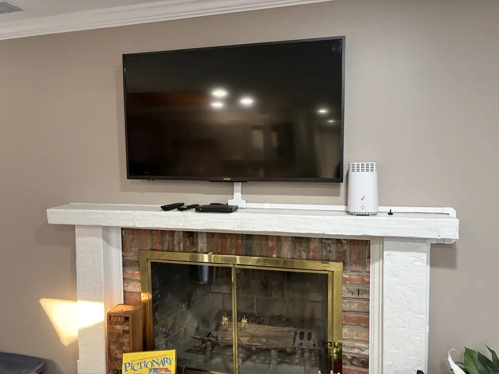 TV above fireplace with board game nearby.